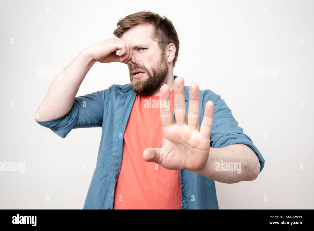 Caucasici, uomo barbuto spreme il naso con la mano a causa di un odore sgradevole e mette il suo palm in avanti, bloccando la fonte del fetore. Isol. Foto Stock