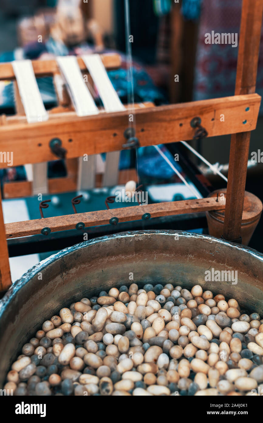 Bozzoli di bachi da seta in acqua calda nel calderone. Tradizionale ruota di filatura macchina per la produzione di seta naturale da baco da seta. Seta procedimento di bobinatura. Foto Stock