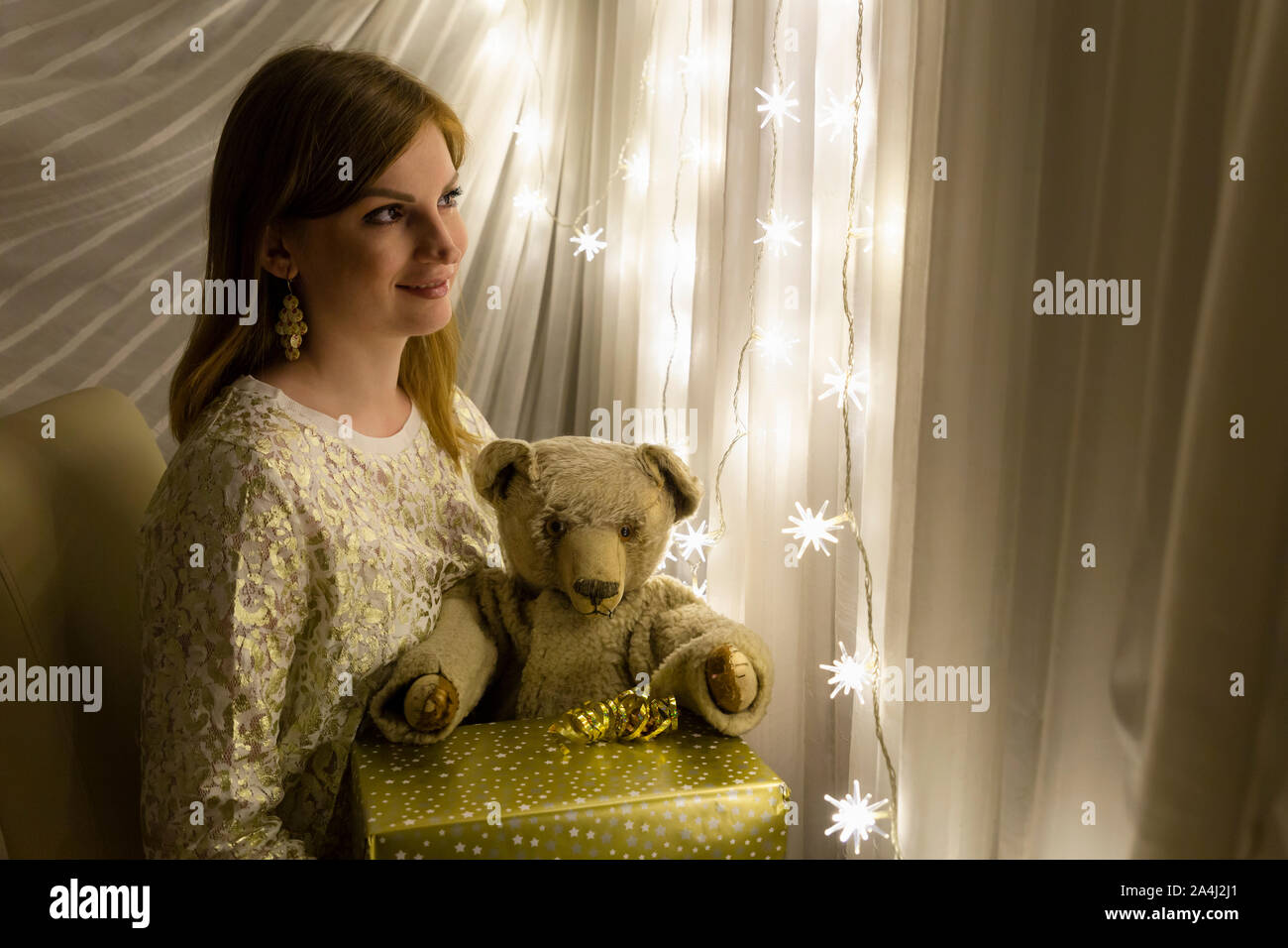 Ritratto di una giovane e bella donna bianca tenendo un orsacchiotto di peluche e un regalo di Natale nelle sue mani nella parte anteriore di una illuminazione a forma di stella di Natale c Foto Stock