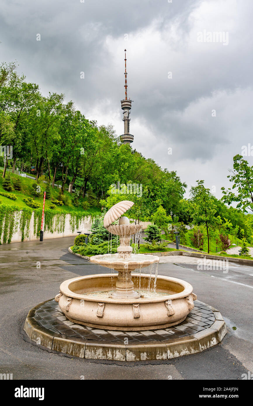 Almaty Kok Tobe Blue Hill Mountain Park con il punto di vista di una fontana con la torre della TV a sfondo su una nebbia e giorno nuvoloso Foto Stock