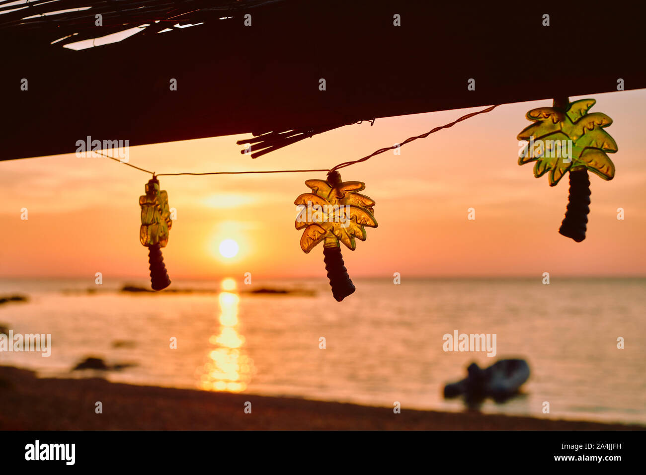 Palm tree a forma di stringa di festa luci decorare un rustico bar sulla spiaggia cafe con un tramonto cielo e mare spiaggia sfondo - tropical beach holiday Foto Stock