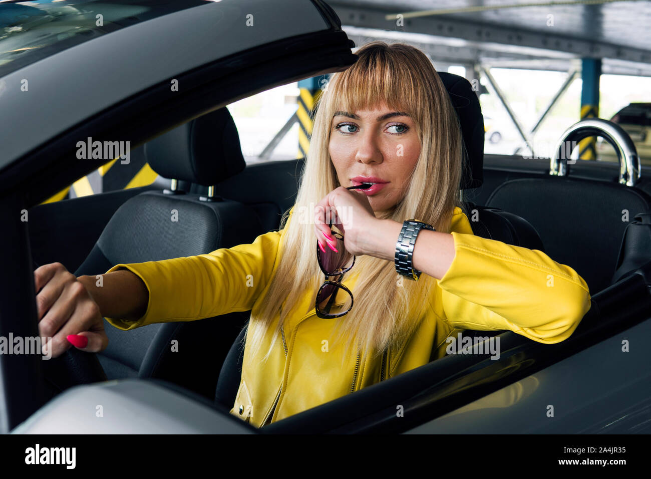 Ragazza bionda in occhiali da sole di guida auto convertibili. moda donna di mordere gli occhiali con un espressione pensosa sul suo volto Foto Stock