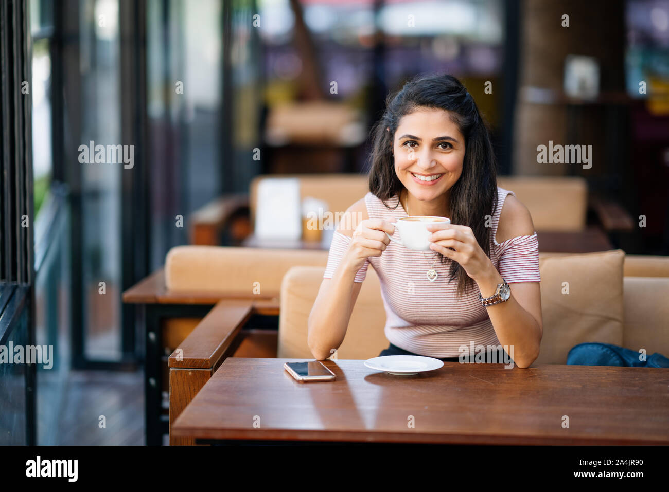 Giovane donna con lo smartphone tenendo tazza di caffè in un bar. Foto Stock