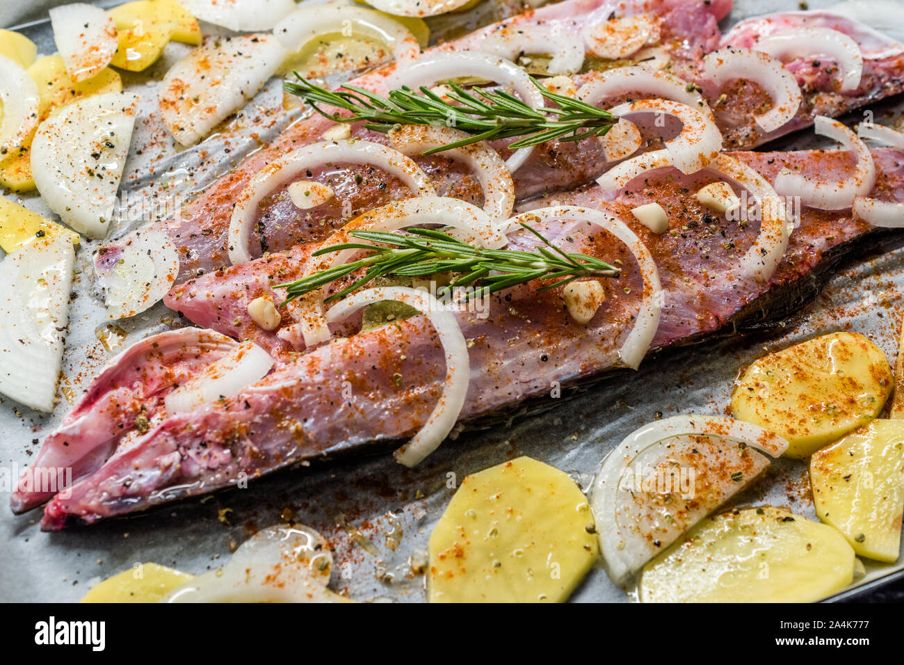 Materie di spigola Filetto di pesce con cipolle, patate e rosmarino nel vassoio da forno con la carta in forno pronto per cucinare. Alimenti biologici. Foto Stock