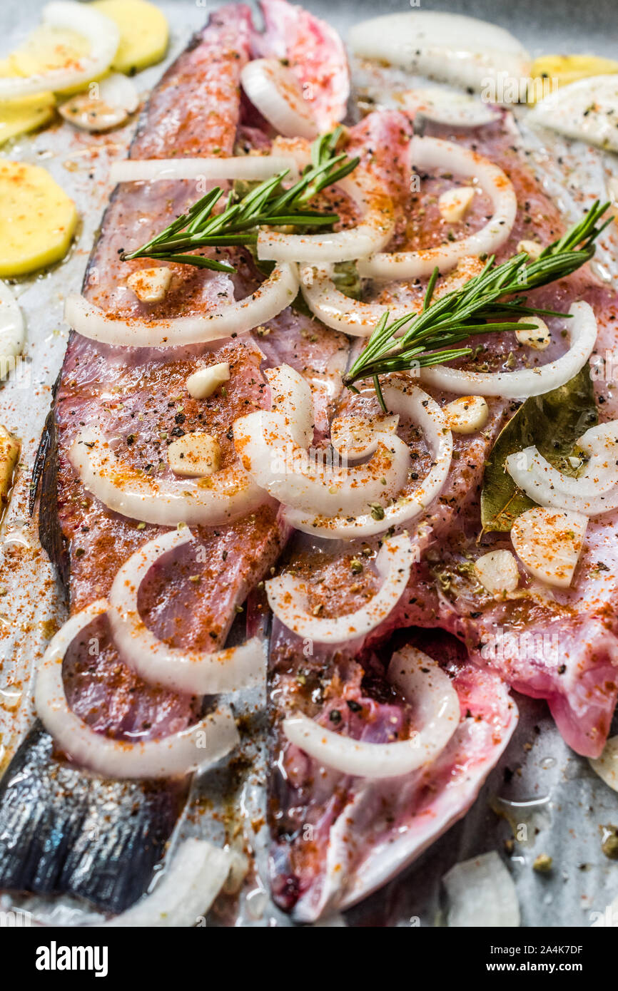 Materie di spigola Filetto di pesce con cipolle, patate e rosmarino nel vassoio da forno con la carta in forno pronto per cucinare. Alimenti biologici. Foto Stock