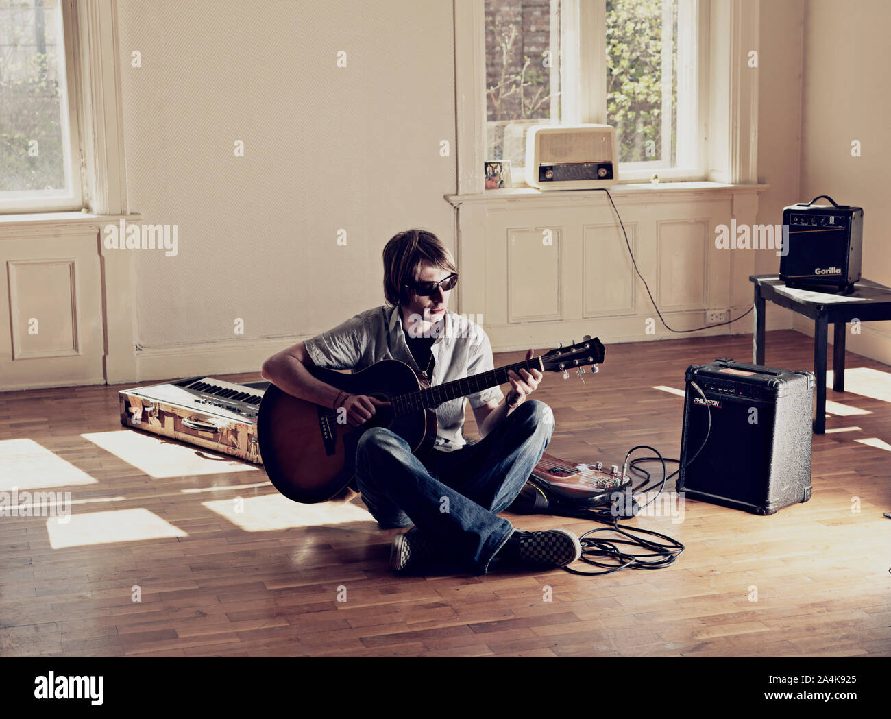 Giovane uomo seduto sul pavimento in parquet a suonare la chitarra Foto Stock