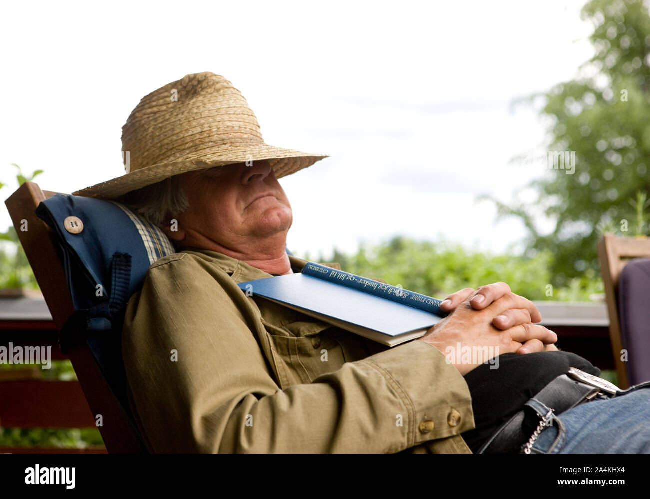 Uomo anziano in appoggio sulla veranda. La faccia coperta dal cappello di paglia. Azienda prenota. Foto Stock