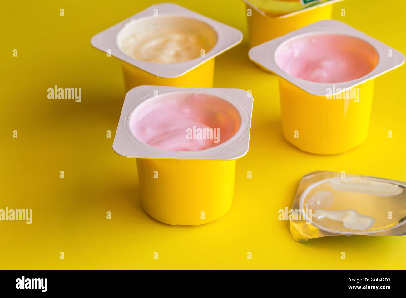 Aromatizzate alla frutta yogurt in giallo bicchieri di plastica sul colore giallo brillante background con lamina d'argento coperchio - tazza di yogurt lo sfondo con il fuoco selettivo Foto Stock