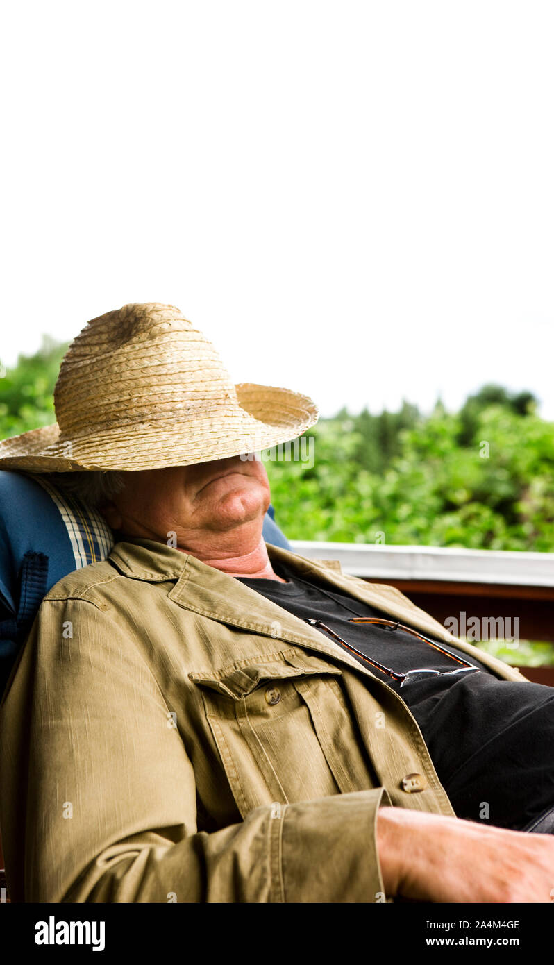 Uomo anziano in appoggio sulla veranda. La faccia coperta dal cappello di paglia. Foto Stock