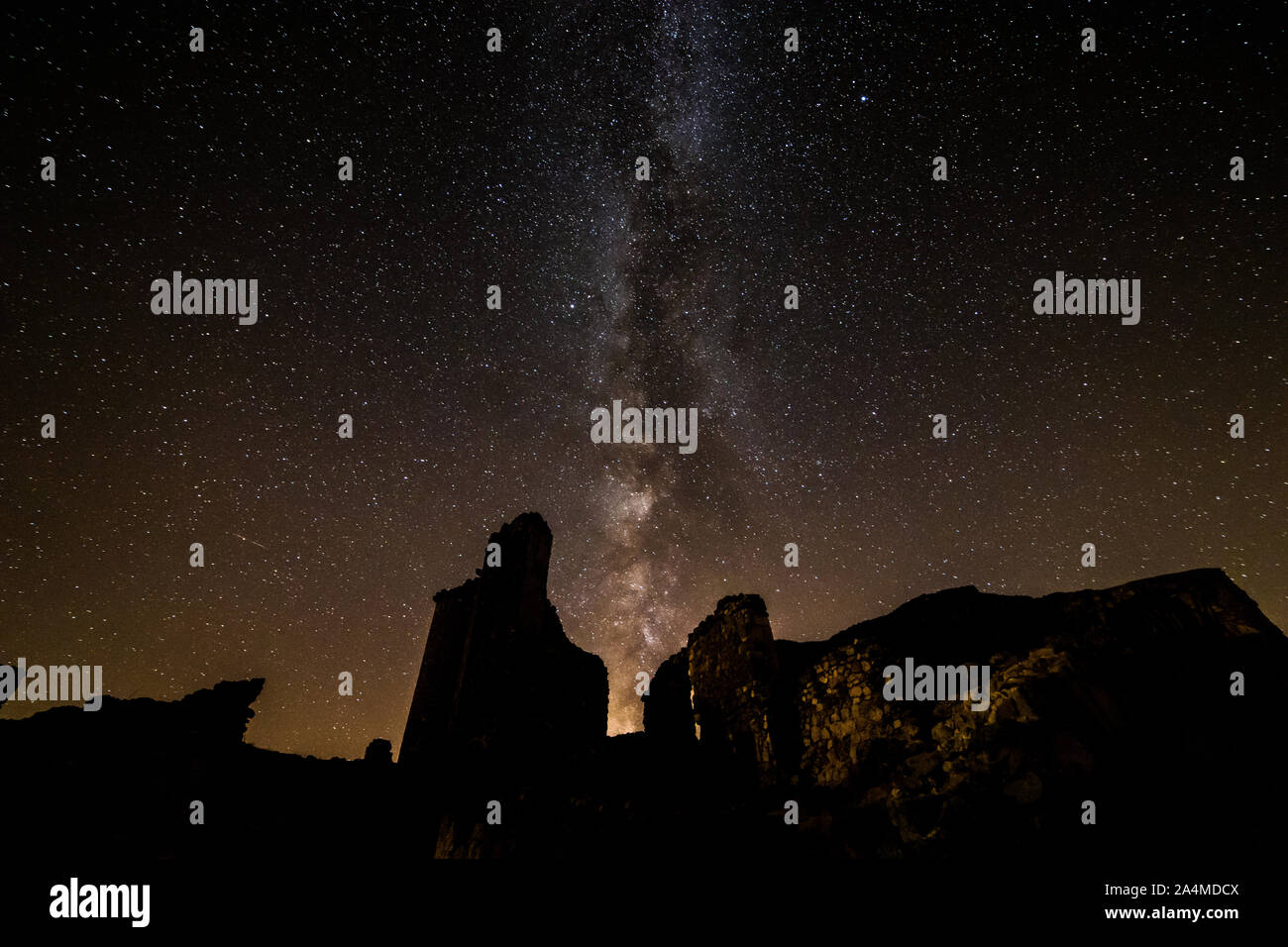 Lunga esposizione fotografia notturna con la Via Lattea in background, tra montagne e vicino ad un edificio con finestre illuminate. Foto Stock