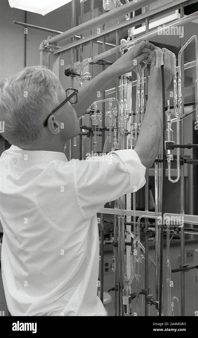 Anni sessanta, storico, un maschio di studente universitario lavora con una serie di provette in vetro fissato su un telaio metallico in un laboratorio di scienze, STATI UNITI D'AMERICA. Foto Stock