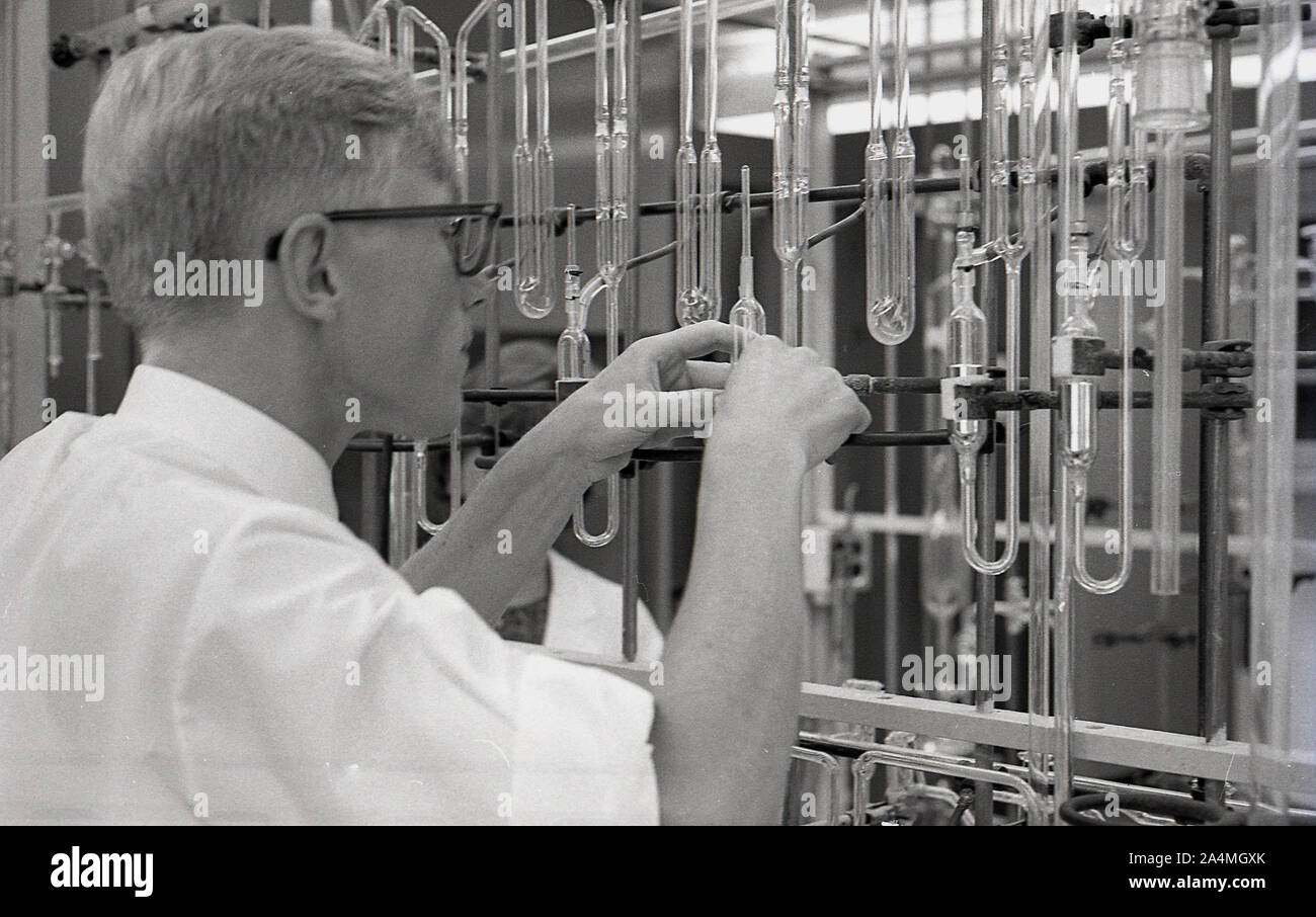 Anni sessanta, storico, un maschio di studente universitario lavora con una serie di provette in vetro fissato su un telaio metallico in un laboratorio di scienze, STATI UNITI D'AMERICA. Foto Stock