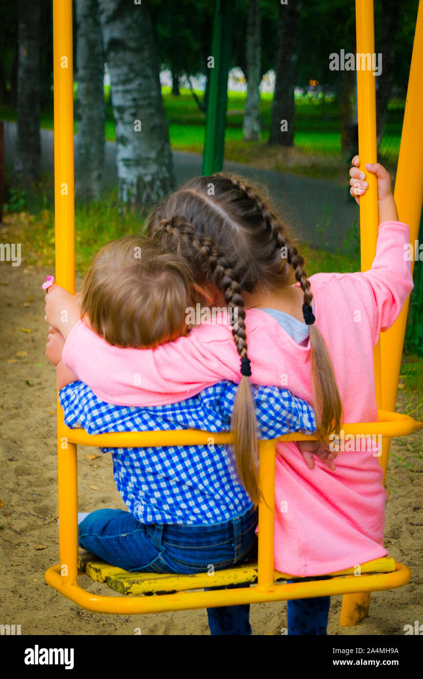 Fratello e sorella che abbracciano giacciono su un altalena in estate. Un paio di bambini seduti su un'altalena nel parco. Foto Stock