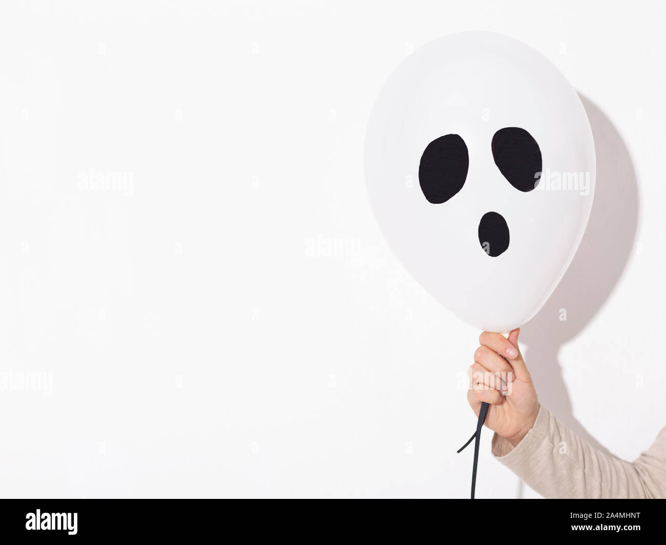 Donna che mantiene il palloncino di halloween ghost in mano su bianco Foto Stock