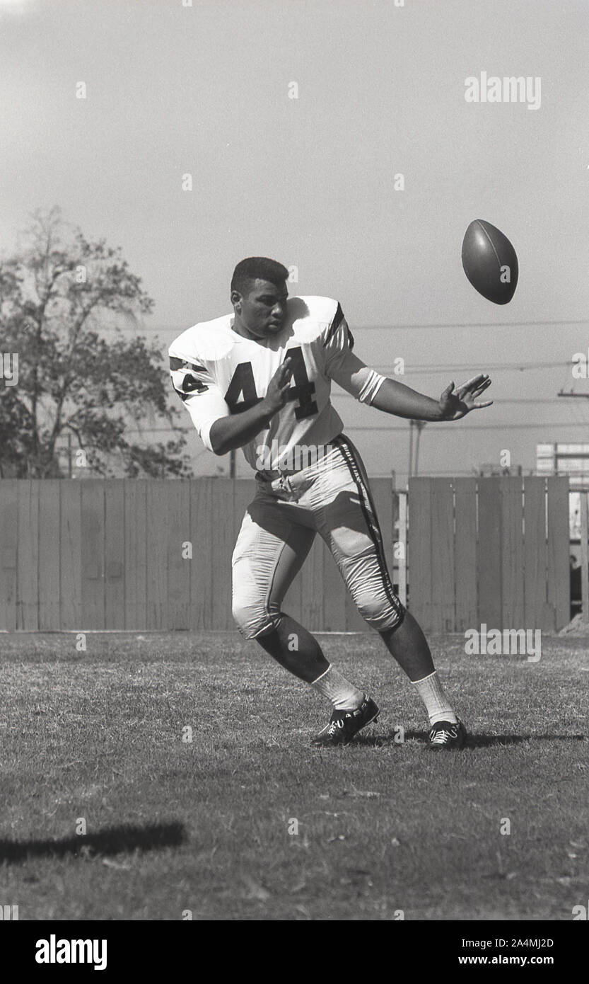 1964, storico, football universitario di Roses, estate e un giovane uomo nero in America che si allena con il pallone alla University of Southern California, Los Angeles, USA. Foto Stock