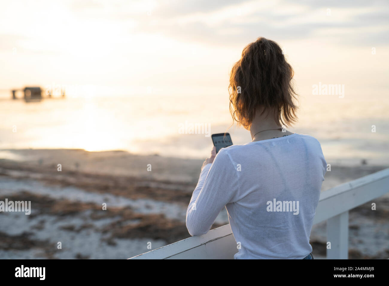 Giovane donna a fotografare il tramonto sulla spiaggia Foto Stock