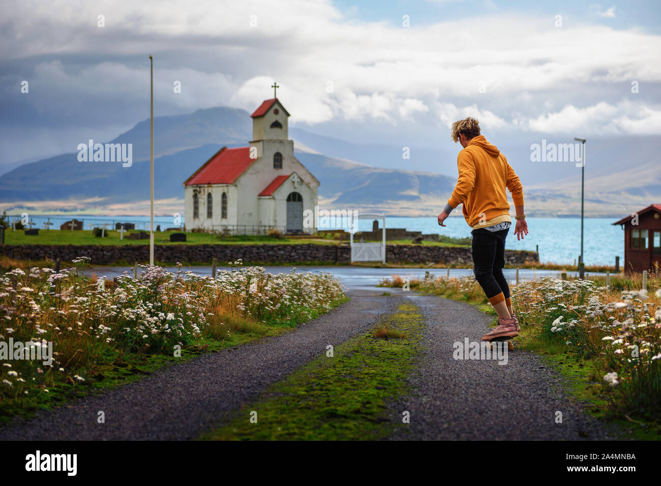 Il giovane skater skateboard verso una chiesa e un cimitero in Islanda Foto Stock