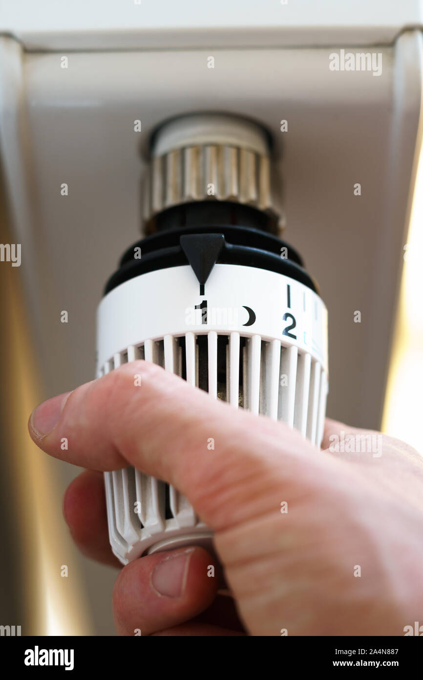 Mano di uomo regolazione valvola del termostato del radiatore fino al numero una icona, simbolo per risparmiare soldi a spese di riscaldamento o impostazione bassa temperatura, closeup, Foto Stock