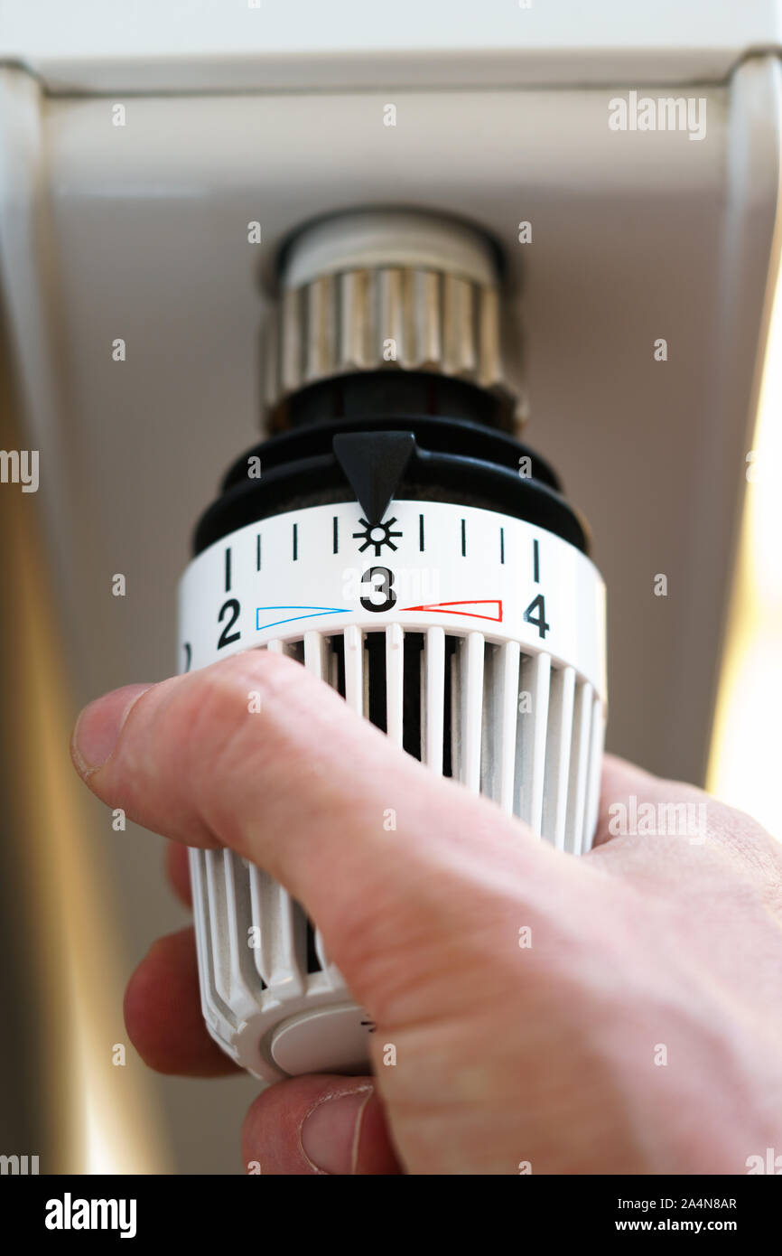 Mano di uomo regolazione valvola del termostato del radiatore al numero tre icona (posizione centrale), simbolo per risparmiare soldi a spese di riscaldamento o la temperatura media Foto Stock