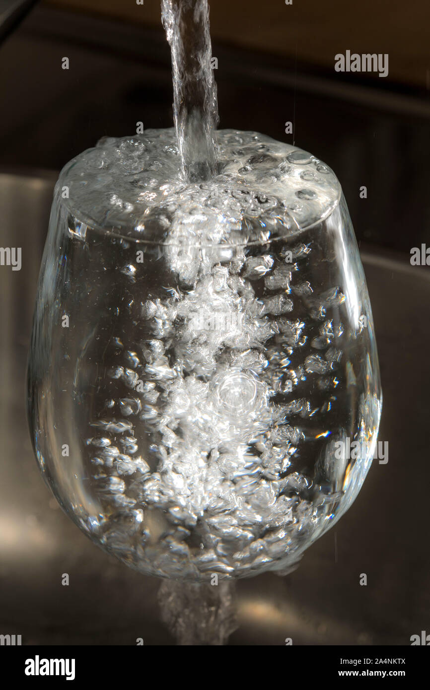 Flussi di acqua da un rubinetto in un bicchiere. Simbolo: il consumo di acqua spreco di acqua. Foto Stock