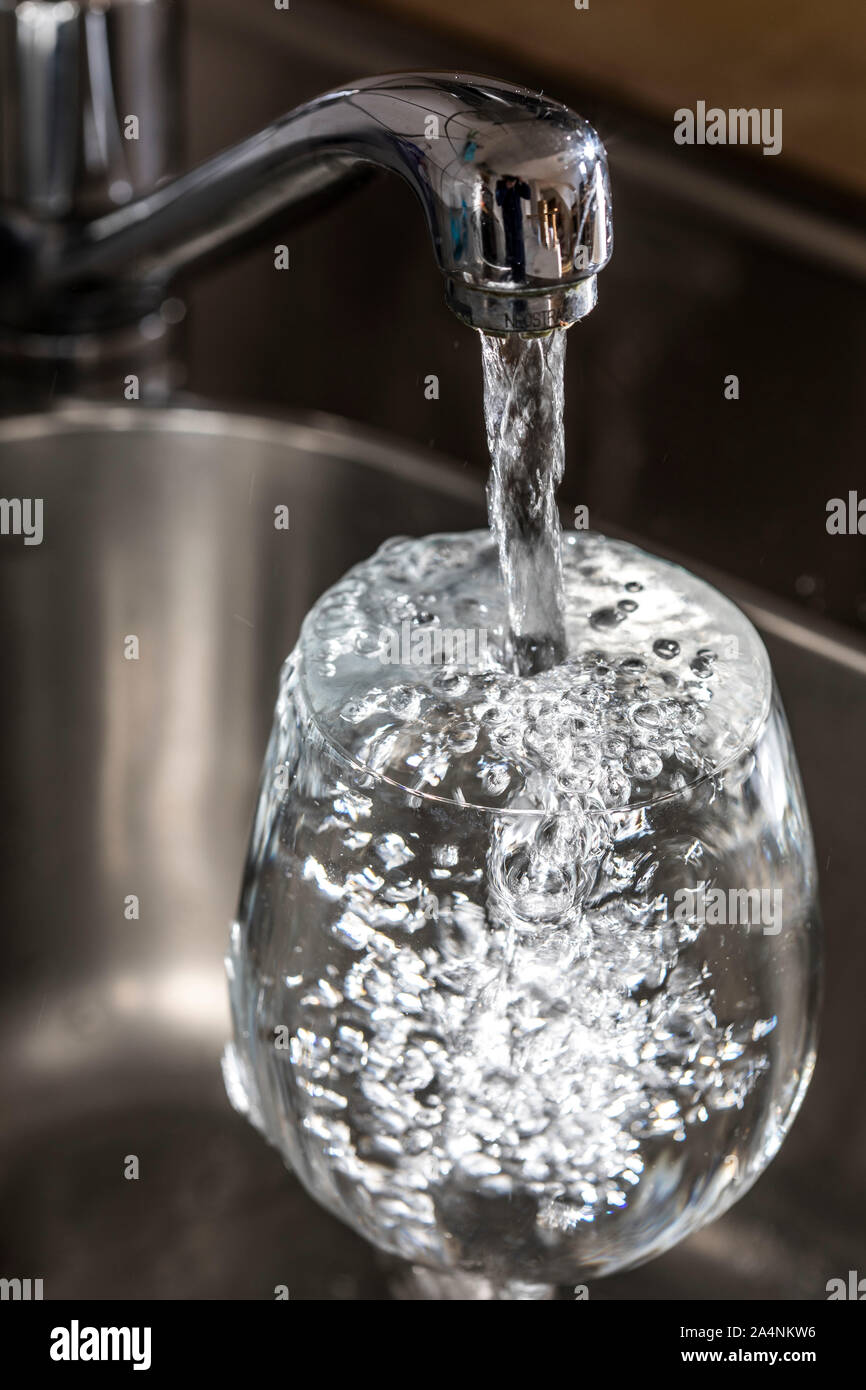 Flussi di acqua da un rubinetto in un bicchiere. Simbolo: il consumo di acqua spreco di acqua. Foto Stock