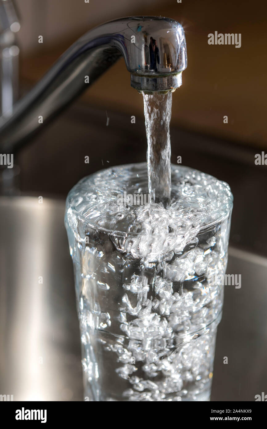Flussi di acqua da un rubinetto in un bicchiere. Simbolo: il consumo di acqua spreco di acqua. Foto Stock