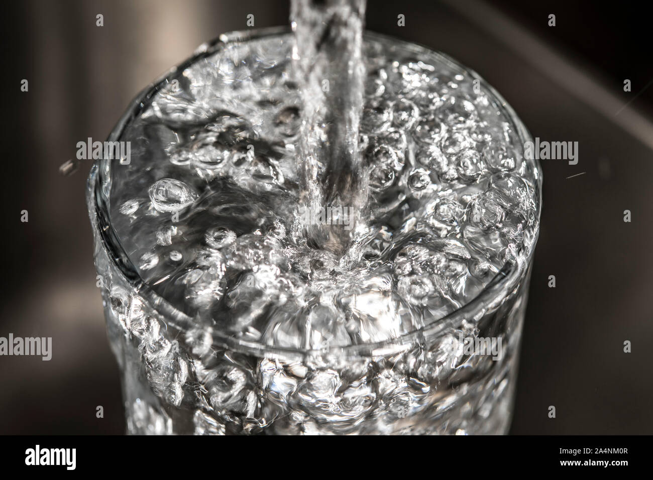Flussi di acqua da un rubinetto in un bicchiere. Simbolo: il consumo di acqua spreco di acqua. Foto Stock
