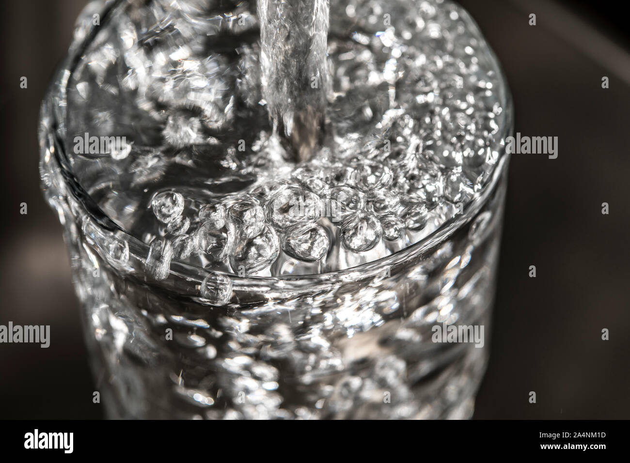 Flussi di acqua da un rubinetto in un bicchiere. Simbolo: il consumo di acqua spreco di acqua. Foto Stock