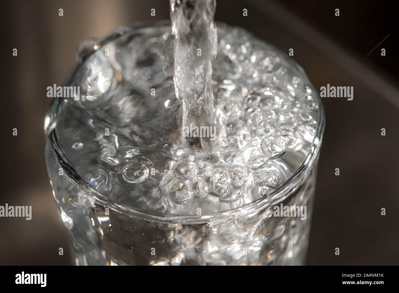 Flussi di acqua da un rubinetto in un bicchiere. Simbolo: il consumo di acqua spreco di acqua. Foto Stock
