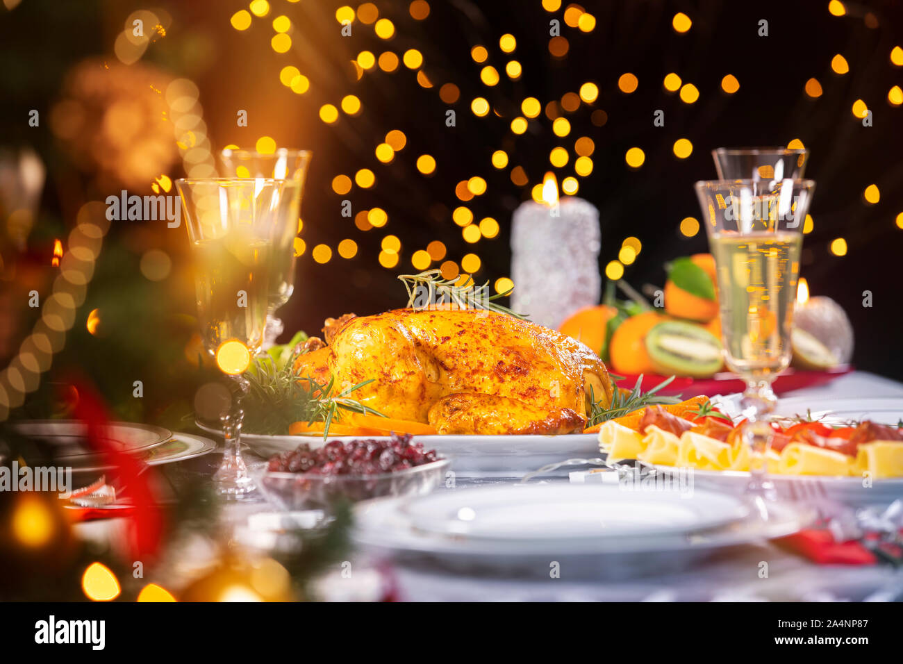 Cena di Natale. Primo piano del gustoso pollo al forno incandescente contro le luci di Natale e candele accese. Vacanza decorate tabella, albero di Natale, Foto Stock
