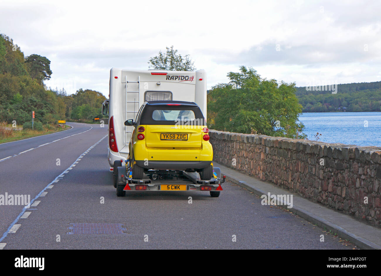 Un Motorhome mobile con il rimorchio attaccato e Smart auto parcheggiate in una piazzola di sosta sulla A82 road da Loch Ness, Scotland, Regno Unito, Europa. Foto Stock