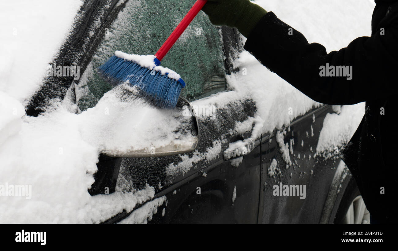 Raschiare la neve di un auto di specchietto retrovisore lato e windows utilizzando la spazzola. Foto Stock