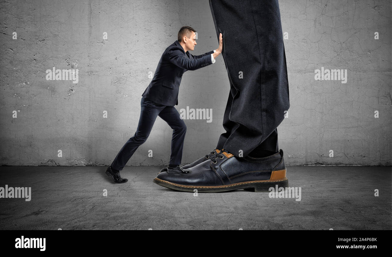 Piccolo imprenditore sta spingendo un big boss del grandi piedi su sfondo grigio Foto Stock
