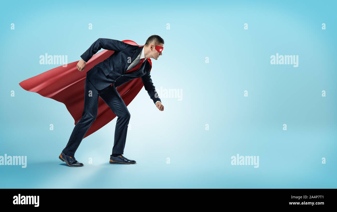 Un imprenditore in un supereroe red cape e una maschera in piedi nella linea di partenza posizione su sfondo blu. Foto Stock