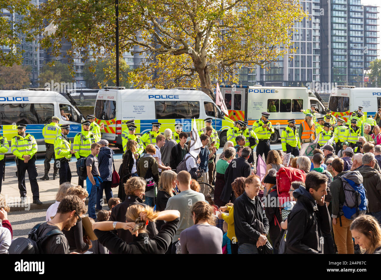 Millbank, London, Regno Unito 15 ottobre 2019; estinzione della ribellione manifestanti con una linea di funzionari di polizia dietro. Fila di furgoni di polizia in background Foto Stock