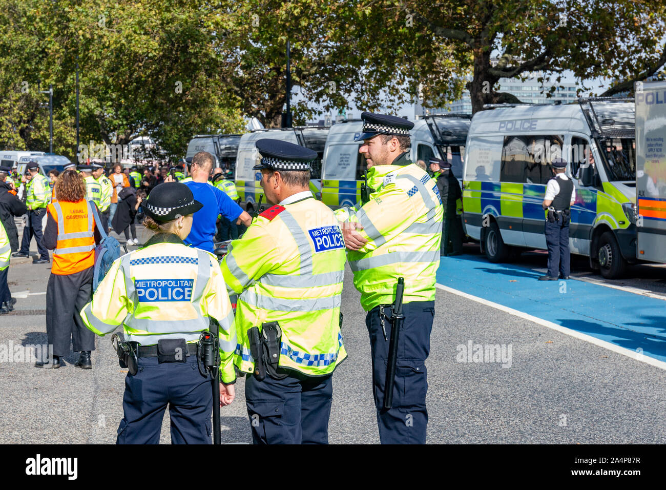 Millbank, London, Regno Unito 15 ottobre 2019; vista posteriore di tre funzionari di polizia in corrispondenza di una ribellione di estinzione protestare con una fila di furgoni di polizia in background Foto Stock