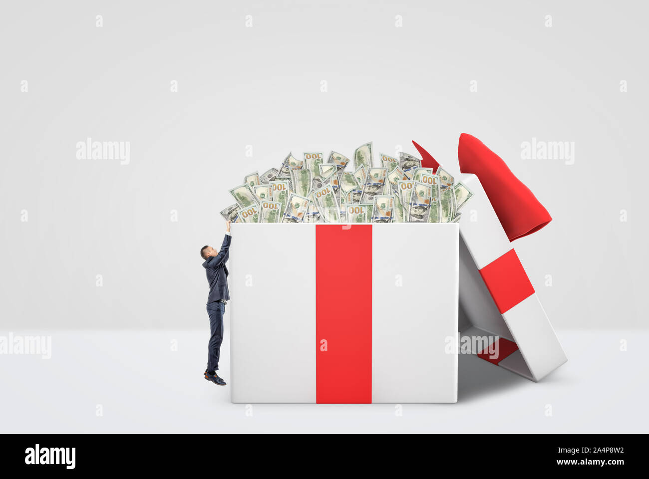 Un piccolo imprenditore che cerca di entrare in un enorme bianco e rosso scatola regalo pieno di denaro. Foto Stock