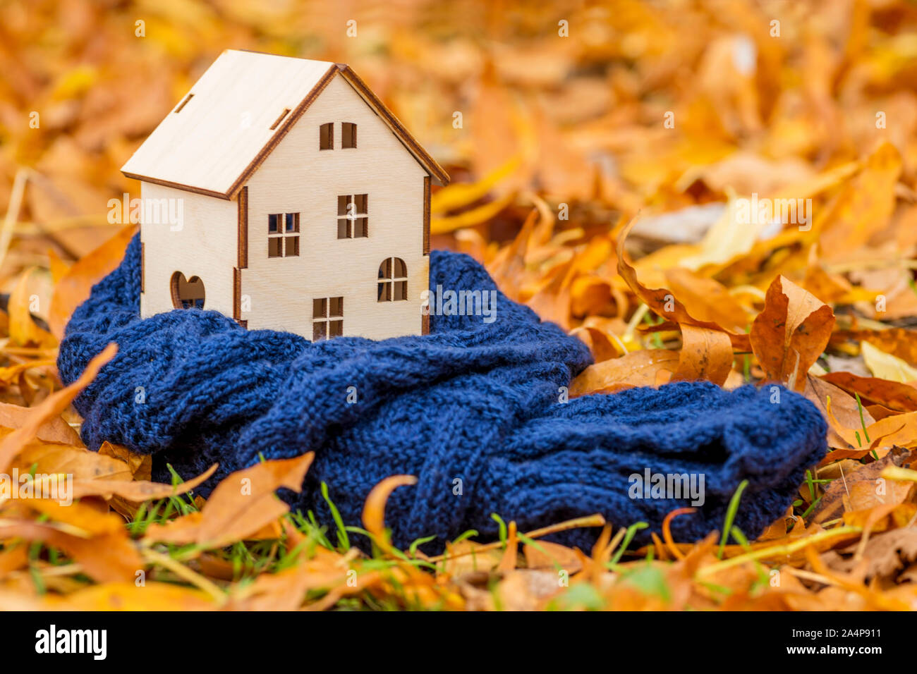 Toy casa di legno è avvolta in una calda sciarpa in foglie di autunno sfondo. Accogliente casa concetto. Foto Stock