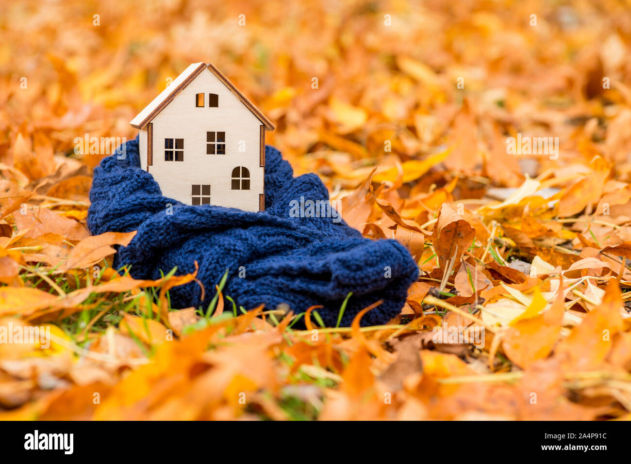 Toy casa di legno è avvolta in una calda sciarpa in foglie di autunno sfondo. Accogliente casa concetto. Foto Stock