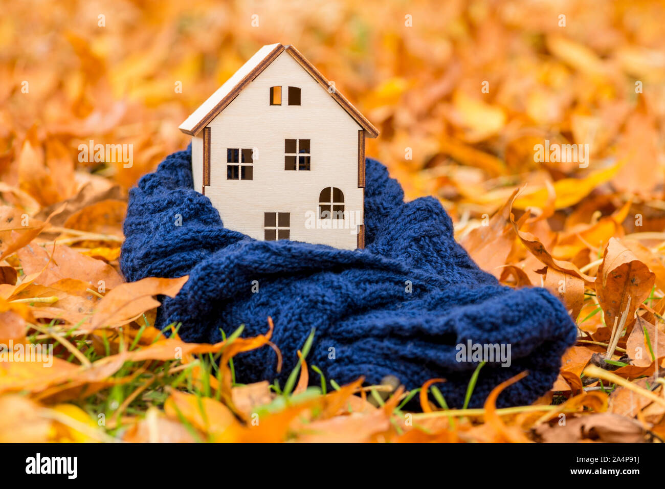 Toy casa di legno è avvolta in una calda sciarpa in foglie di autunno sfondo. Accogliente casa concetto. Foto Stock