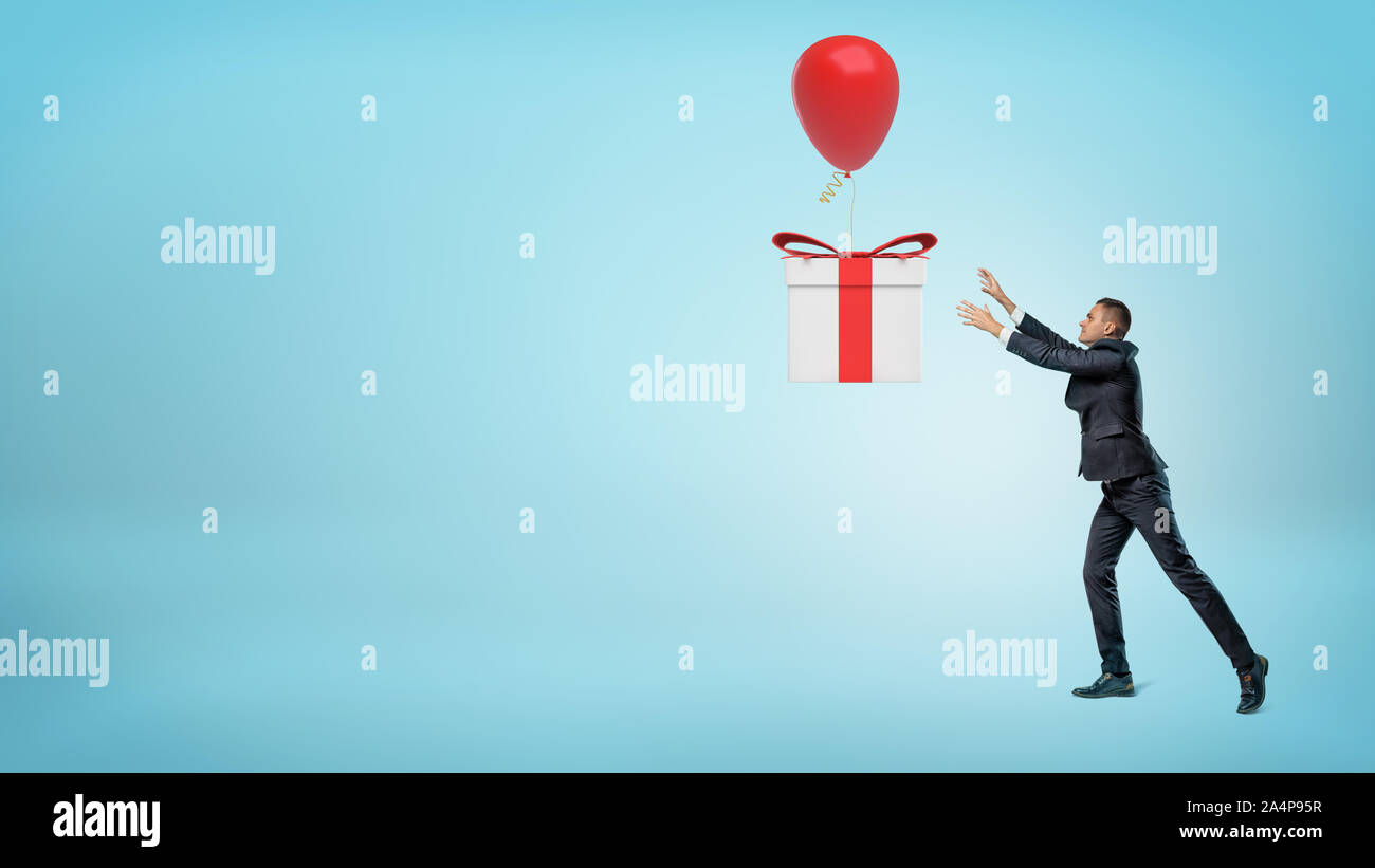 Un piccolo imprenditore che cerca di catturare un grande regalo che è volare lontano su un palloncino. Foto Stock