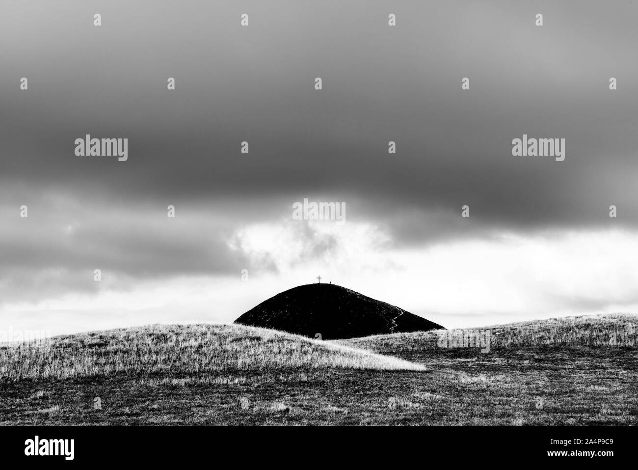 Montagna nera con crocifisso in cima tra le colline - paesaggio italiano Foto Stock