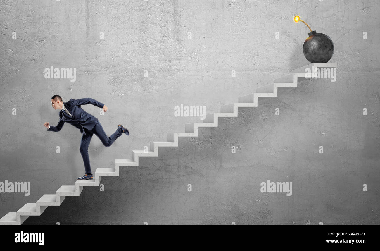 Un imprenditore paura correre giù di cemento grigio scale lontano da una grande bomba di ferro con un fusibile di lit. Foto Stock