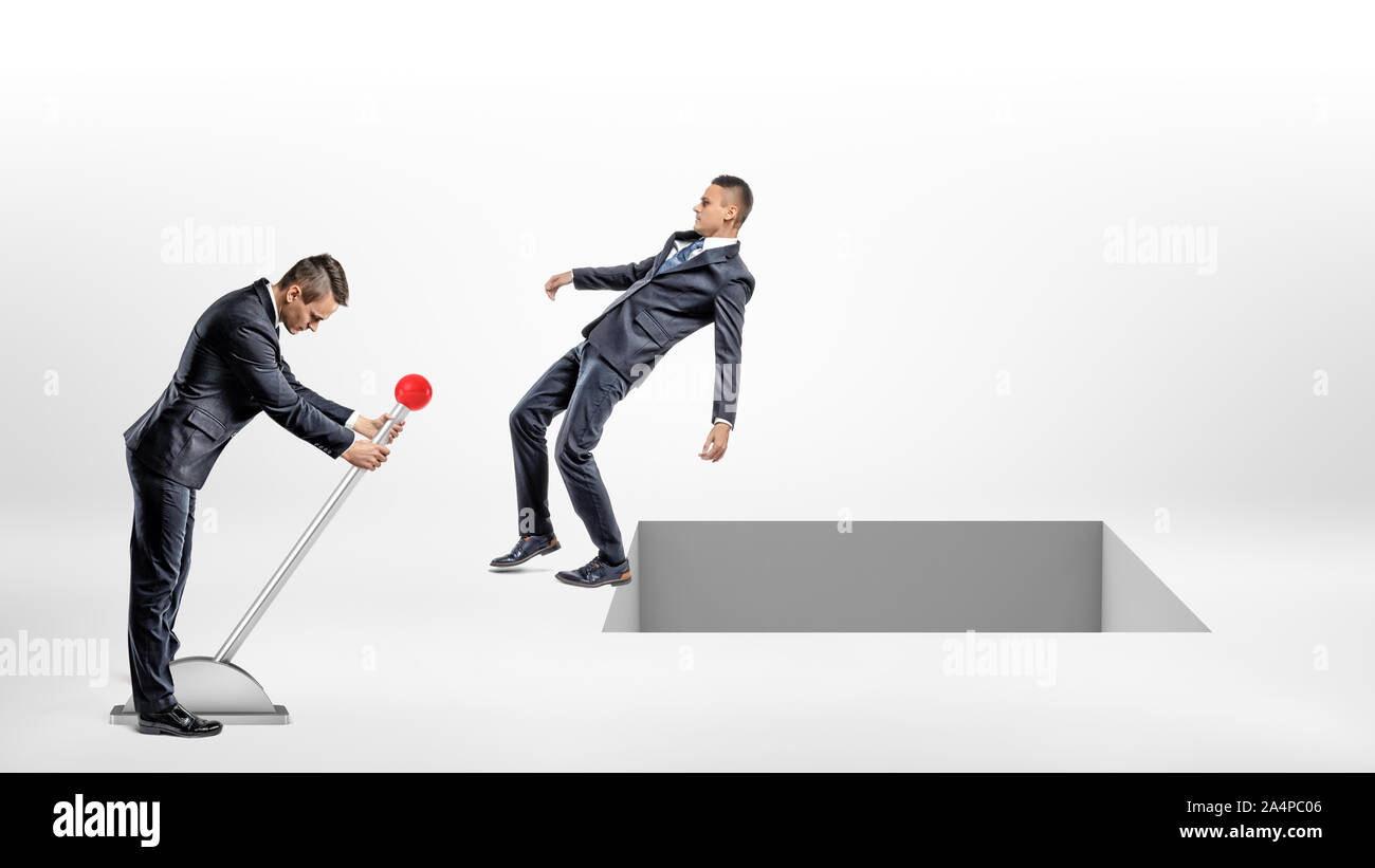 Un imprenditore diventa una grande interruttore leva mentre un altro uomo cade indietro per aprire un foro quadrato nel terreno. Foto Stock