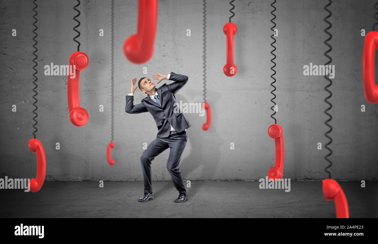Una paura imprenditore su sfondo concreto pelli da molti retro rosso i ricevitori del telefono che pendono sul loro corde. Foto Stock