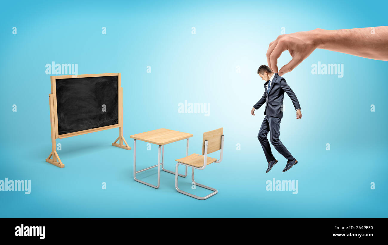 Un piccolo uomo d affari pendenti da una gigantesca mano su sfondo blu con arredi e di una lavagna. Foto Stock