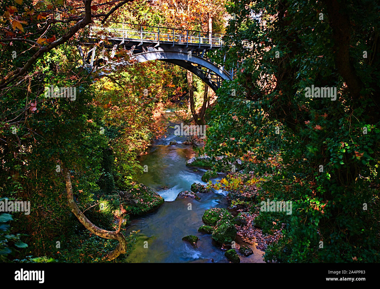 Una lunga esposizione foto, del bel fiume con alberi e il vecchio ponte metallico, Kalavryta Peloponneso, Grecia. Foto Stock