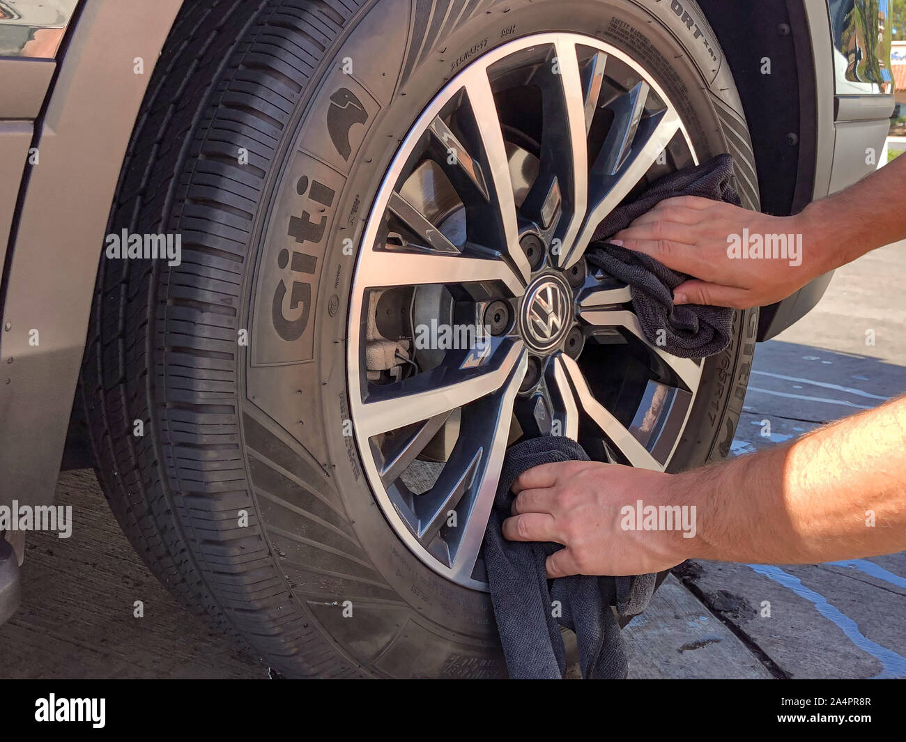 Uomo di pulitura a mano la ruota e il pneumatico con nero panno in microfibra. Salvietta giù i cerchioni lucida la superficie della vettura. Dettagli auto e lavaggio auto concept , San Diego, Stati Uniti d'America, Ottobre 11th, 2019 Foto Stock