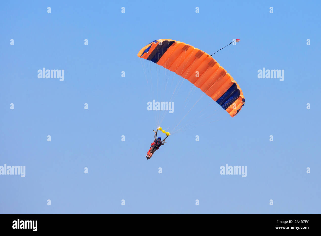 Paracadutista sotto un paracadute arancione nel cielo blu Foto Stock