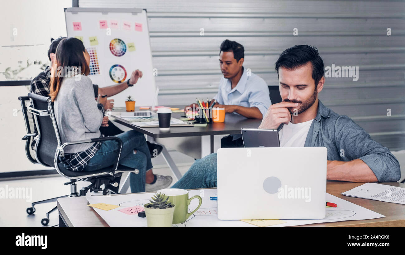 Creative designer direttore il controllo del lavoro sul computer portatile mentre il team è in riunione informale a sfondo in un ufficio moderno.agenzia stile di vita il concetto di lavoro Foto Stock